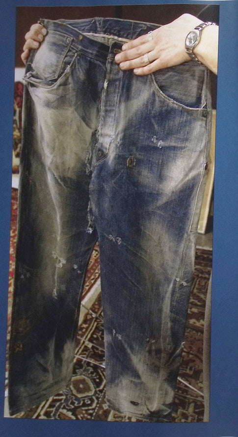 Distressed dark blue jeans with rips and fading, displayed on mannequin with hands.